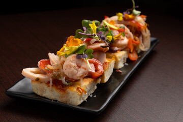 Delicious seafood bruschetta with shrimps and edible flowers on black plate