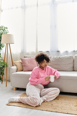 Fototapeta premium A young woman relaxes on the floor with a cup, soaking in the comfort of her home.