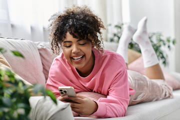 A cheerful woman relaxes on the couch, happily engaging with her mobile device.