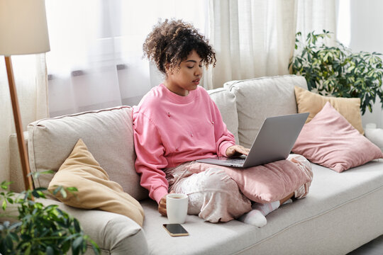 A woman sips coffee while focused on her laptop in a sunny living room.