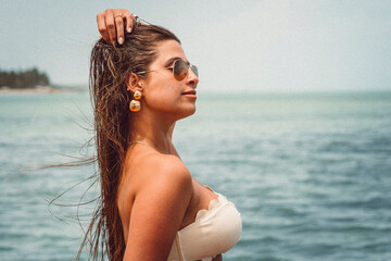 Beautiful face woman bikini model wearing aviator sunglasses and golden jewelry at the beach in northeast brazil