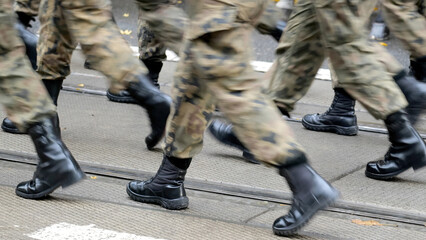 Anonymous army soldiers marching through the street in generic camo uniforms and black boots,...
