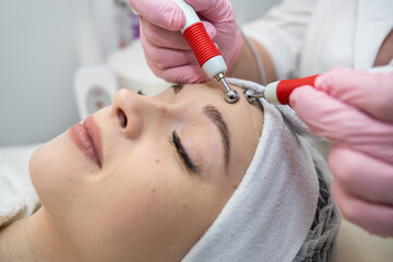 Naklejka premium Young pretty woman receiving stimulating electric facial treatment from therapist at spa clinic