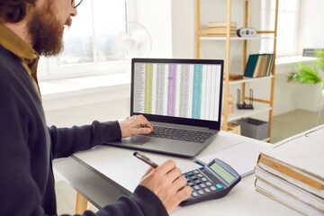 Fototapeta premium Financial accountant working with business sheets. Adult man sitting at office desk, using laptop computer and calculator and working with electronic spreadsheet files