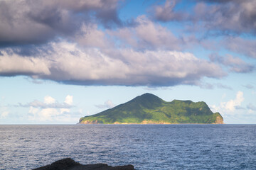 Distant view of Turtle Island standing in the sea, covered in lush green plants. White clouds...
