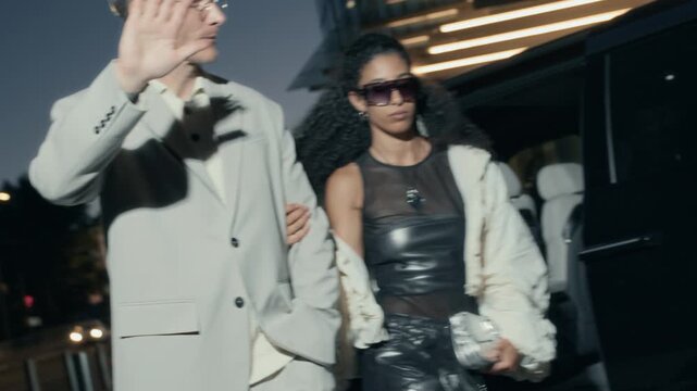 Famous interracial celebrity couple hiding their faces from paparazzi while getting out of car and walking down street to event at night