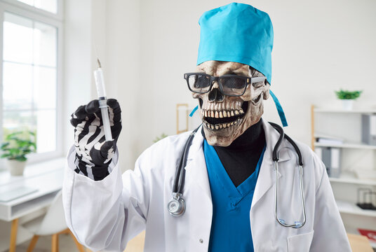 Doctor in evil skeleton mask, glasses, scrubs cap, white coat, with syringe in hand shows anti vaxxer fears, death, deadly vaccine hazard, bad pharmaceutical industry, pain, harmful treatment concepts