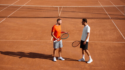 Two men, tennis players meeting on outdoor court, discussing strategy before the game, preparing for intensive training session. Concept of sport, competition, active and healthy lifestyle