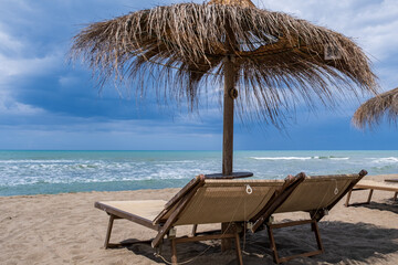 Sea shore with dark clouds and straw umbrellas in Tuscany, Italy