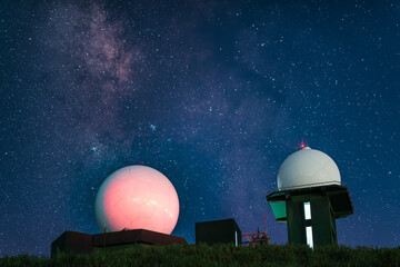 White meteorological radar station with blinking lights set against a deep blue starry sky and a...