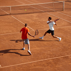 Two men, tennis players in motion on outdoor clay court, showing game skills and teamwork cooperation, playing with focus. Concept of sport, competition, active and healthy lifestyle