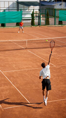 Vertical image of two men, tennis players in motion on clay court, showing competitive game and readiness to make move. Concept of sport, competition, active and healthy lifestyle
