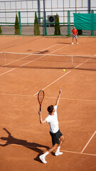 Vertical image of two men, tennis players on clay court playing, training, getting ready to serve and receive ball. Intense summer day game. Concept of sport, competition, active and healthy lifestyle