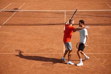 Happy positive men, friends, tennis players embracing each other after good intense game on outdoor...