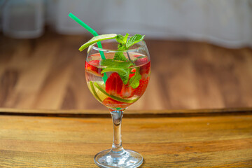 Glass with fruit cocktail strawberry mint lime with ice on wooden table