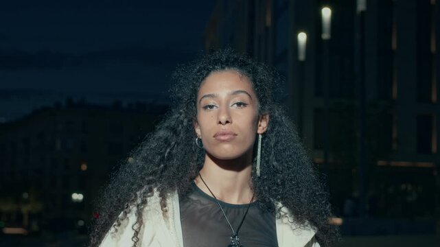 Slowmo portrait of stunning Biracial female celebrity taking off black sunglasses and posing for camera in city lights at night