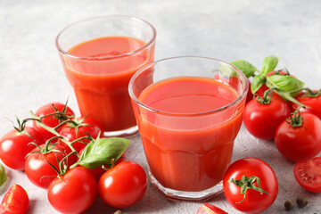 Tasty tomato juice in glasses, basil leaves and fresh vegetables on light grey table