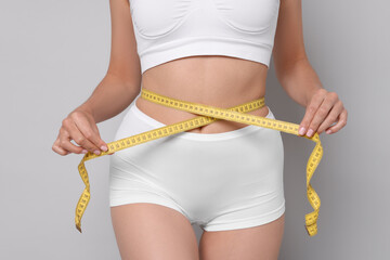 Diet and weight loss concept. Woman with measuring tape showing her slim body against light grey...