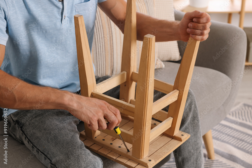 Wall mural Man repairing wooden stool with screwdriver indoors, closeup