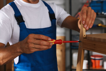 Man repairing wooden stool with screwdriver indoors, closeup