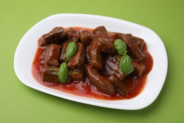 Tasty stew with okra, tomato sauce and basil on light green background, closeup