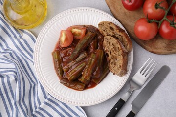 Tasty stew with okra, tomato sauce and bread on white table, flat lay