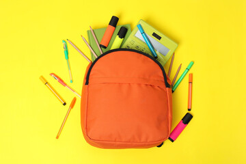 Orange backpack and different school supplies on yellow background, flat lay