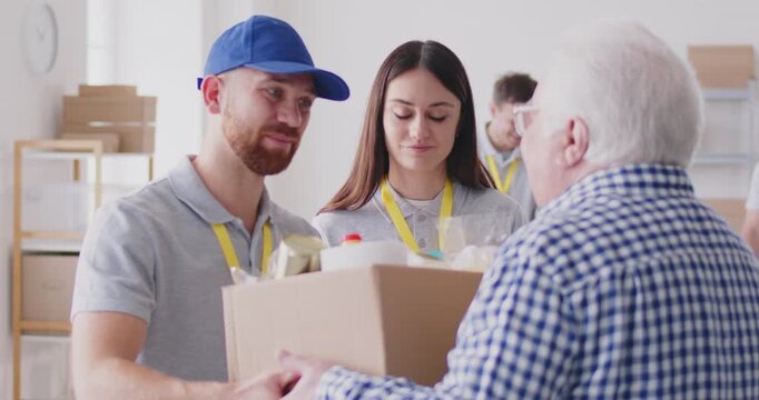 Joyful volunteer team offers a box of food and humanitarian assistance to an elderly pensioner. Their act embodies the values of donation, charity, community service, and compassionate help.