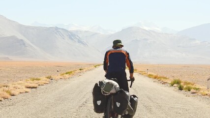 Back view adventurous caucasian male traveler cycle bicycle touring solo on asphalt famous Pamir highway M41 road in remote high Pamir mountains. Pamir highway adventure travel route destination