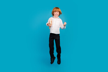 Full body portrait of little schoolchild boy jump hold book wear uniform isolated on blue color background