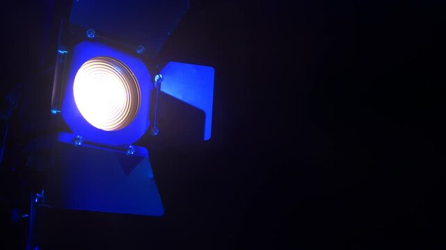 Theater spotlight with a fresnel lens with curtains on a black background with blue reflections. save space. Medium plan.