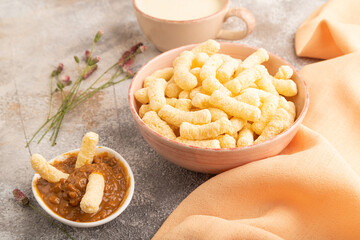 Corn flakes sticks with caramel in ceramic bowl on gray concrete, side view, close up.