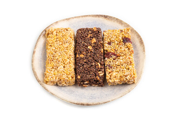 Granola bars with caramel, nuts, flakes in ceramic plate isolated on white. Side view, close up.