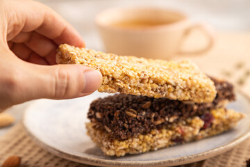 granola bars with caramel, nuts, flakes in ceramic plate on brown concrete with hand. Side view, selective focus.