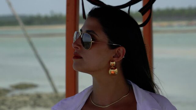 Beautiful face woman bikini model wearing sunglasses and golden jewelry at the beach in northeast brazil