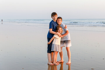 Three children, happy siblings on ocean beach at sunset. happy family, two school boys and one little preschool girl. Brothers and sister having fun, Spain, Costa del Sol