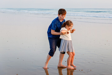 Two children on ocean beach. Teenager boy and little preschool sister having fun by sunset. Sea vacation for family. Siblings laughing and smiling. Happiness and love.