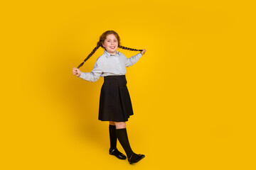 Full body photo of cute little schoolgirl pull hair braids playful funky dressed stylish uniform isolated on yellow color background