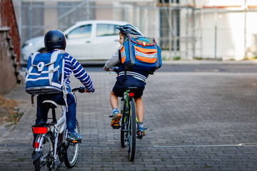 Two school kid boys in safety helmet riding with bike in the city with backpacks. Happy children in colorful clothes biking on bicycles on way to school. Safe way for kids outdoors to school