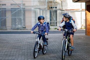 Two school kid boys in safety helmet riding with bike in the city with backpacks. Happy children in colorful clothes biking on bicycles on way to school. Safe way for kids outdoors to school
