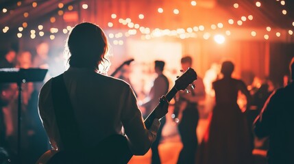 A guitarist performs on stage while attendees dance and socialize in a warmly lit venue adorned with string lights.