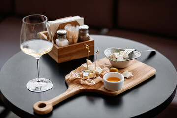 Glass of white wine is served with a cheese platter on a wooden board, creating an inviting atmosphere for a sophisticated snack or appetizer