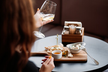 Person seated at a table holding a glass of white wine with a plate of food and condiments in front elegant restaurant setting top-down angle medium plan