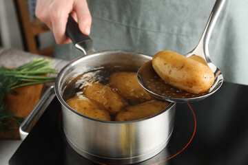 Woman taking boiled potato from saucepan on stove, closeup