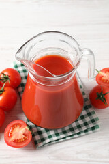 Tasty tomato juice in glass jug and fresh vegetables on white wooden table