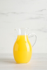Fresh orange juice in glass jug on white wooden table