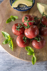 Fresh dark red vine tomatoes on a wooden board with basil leaves close up