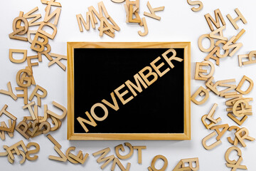 Wooden board with the name of the month "November" written on it and scattered letters next to it