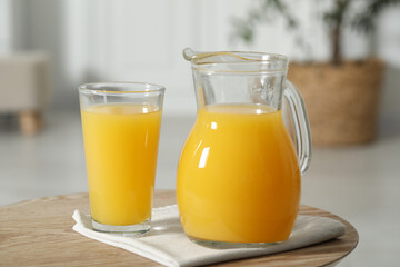 Tasty orange juice in jug and glass on wooden table, closeup