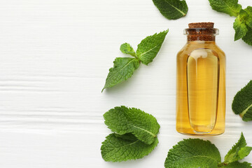 Bottle of essential oil and mint on white wooden table, flat lay. Space for text